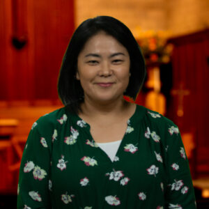 Yui Teryua, Administrative Assistant - Photo of young woman standing in a church wearing a green and white floral shirt.  Foundation Overview